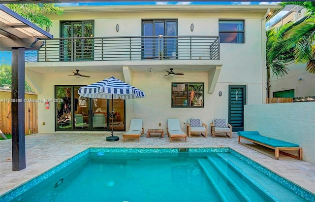 rear view of house featuring ceiling fan, a balcony, and a fenced in pool