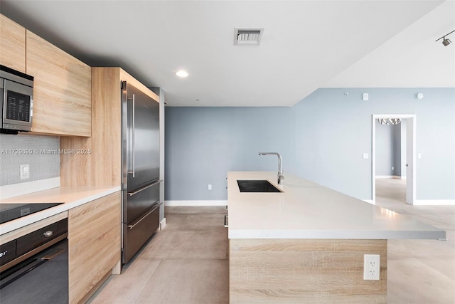 kitchen featuring sink, black appliances, tasteful backsplash, and an island with sink