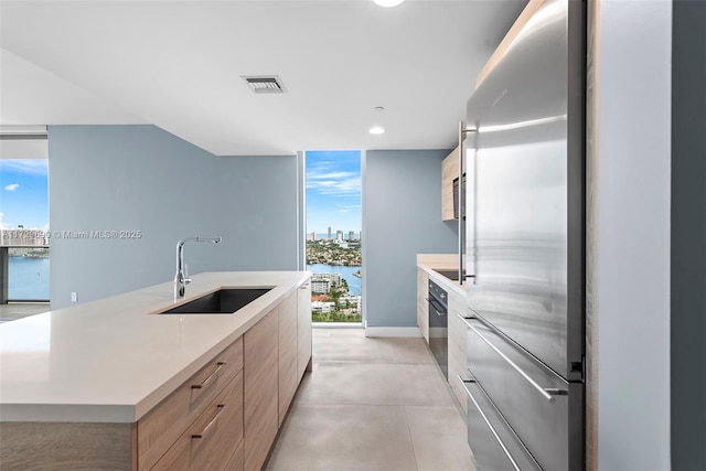 kitchen featuring sink, a water view, a center island with sink, high end refrigerator, and black oven