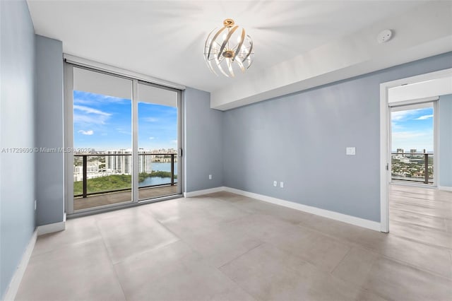 unfurnished room featuring a chandelier, a wealth of natural light, a wall of windows, and a water view