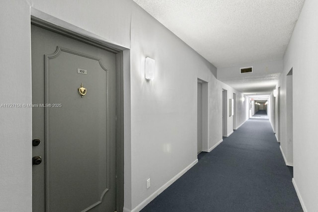 hallway with dark colored carpet and a textured ceiling