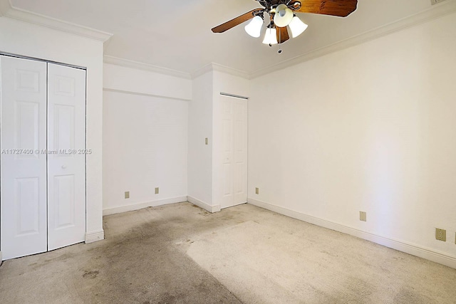 unfurnished bedroom with ornamental molding, ceiling fan, light colored carpet, and multiple closets