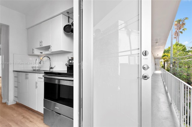 kitchen with white cabinets, sink, decorative backsplash, and stainless steel electric stove