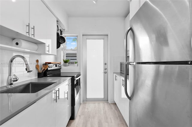 kitchen featuring white cabinetry, stainless steel appliances, sink, backsplash, and light hardwood / wood-style flooring