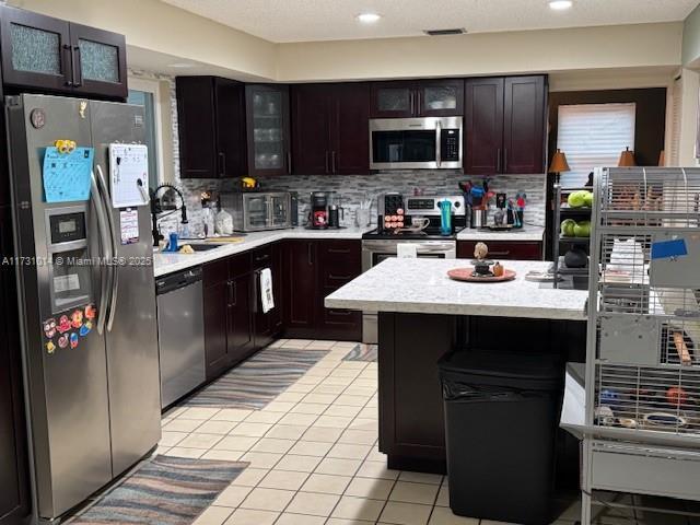 kitchen with appliances with stainless steel finishes, sink, backsplash, light tile patterned floors, and a kitchen island