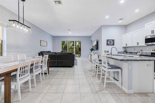 kitchen featuring white cabinets, appliances with stainless steel finishes, decorative light fixtures, dark stone counters, and sink