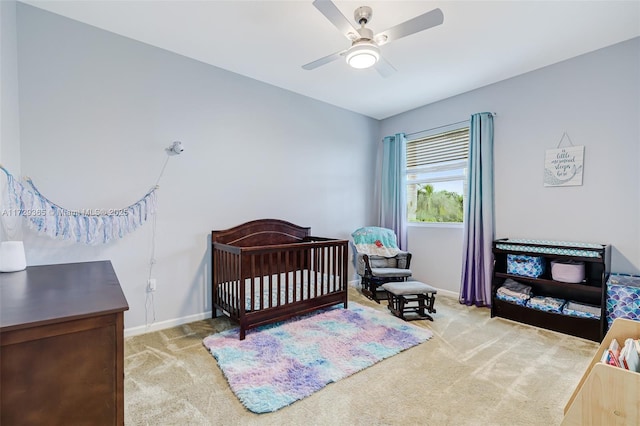 carpeted bedroom with ceiling fan and a nursery area