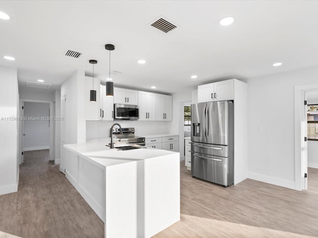 kitchen featuring appliances with stainless steel finishes, white cabinetry, hanging light fixtures, light hardwood / wood-style flooring, and kitchen peninsula