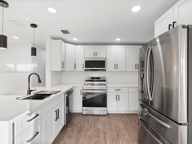 kitchen featuring pendant lighting, hardwood / wood-style floors, white cabinetry, stainless steel appliances, and sink