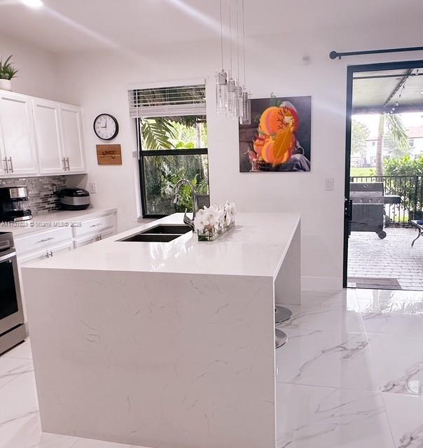 kitchen featuring decorative light fixtures, sink, white cabinets, a center island with sink, and decorative backsplash