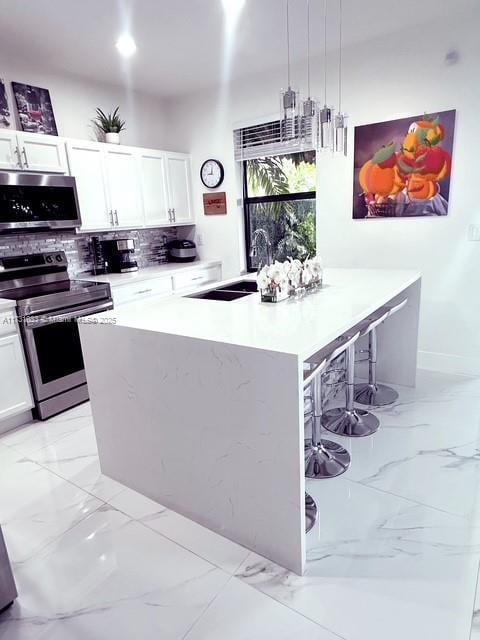 kitchen with hanging light fixtures, white cabinetry, a kitchen bar, decorative backsplash, and stainless steel appliances