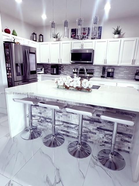 kitchen with white cabinetry, decorative backsplash, decorative light fixtures, stainless steel appliances, and a breakfast bar area