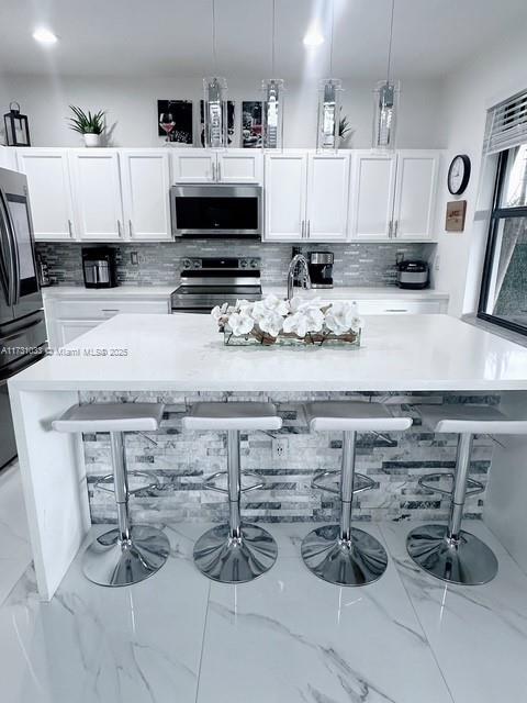 kitchen featuring decorative light fixtures, tasteful backsplash, white cabinetry, and stainless steel appliances