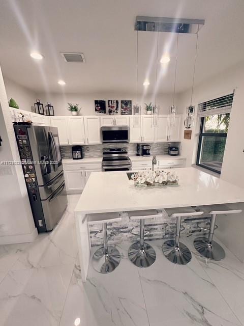 kitchen featuring decorative light fixtures, white cabinetry, stainless steel appliances, and a breakfast bar area