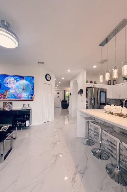 interior space featuring white cabinetry, backsplash, hanging light fixtures, and stainless steel fridge with ice dispenser