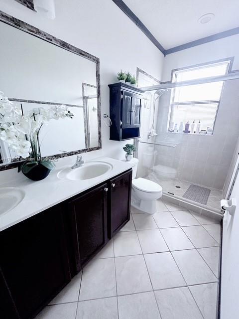 bathroom with tile patterned flooring, vanity, toilet, a tile shower, and crown molding