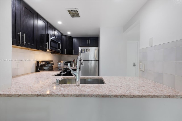 kitchen with sink, light stone counters, appliances with stainless steel finishes, kitchen peninsula, and backsplash