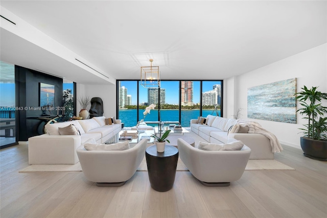 living room with expansive windows, a water view, an inviting chandelier, and light hardwood / wood-style flooring