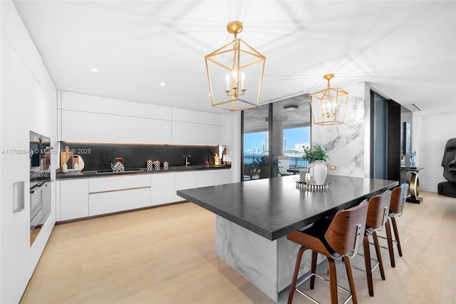 kitchen featuring white cabinetry, pendant lighting, light hardwood / wood-style floors, and a breakfast bar