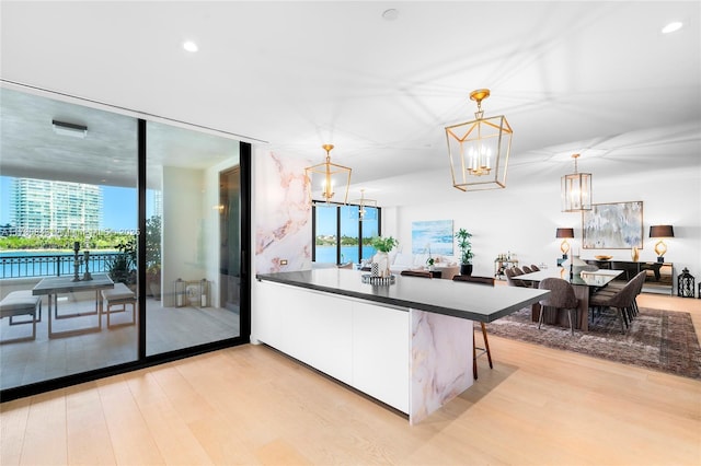 kitchen with hanging light fixtures, a notable chandelier, light hardwood / wood-style floors, white cabinets, and a kitchen bar