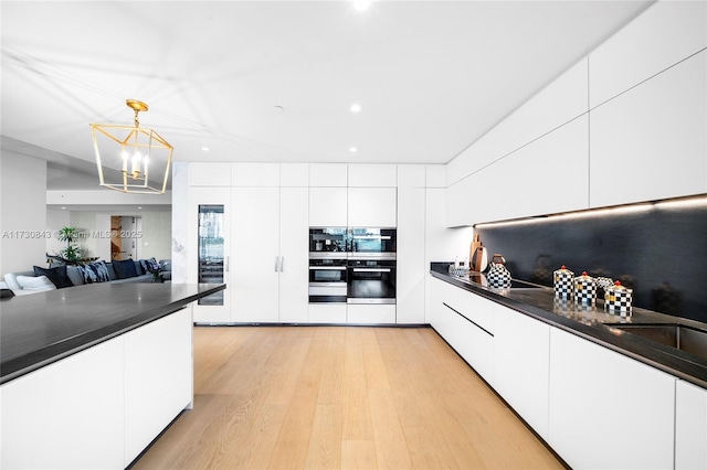 kitchen featuring white cabinetry, black electric cooktop, pendant lighting, stainless steel double oven, and light hardwood / wood-style floors