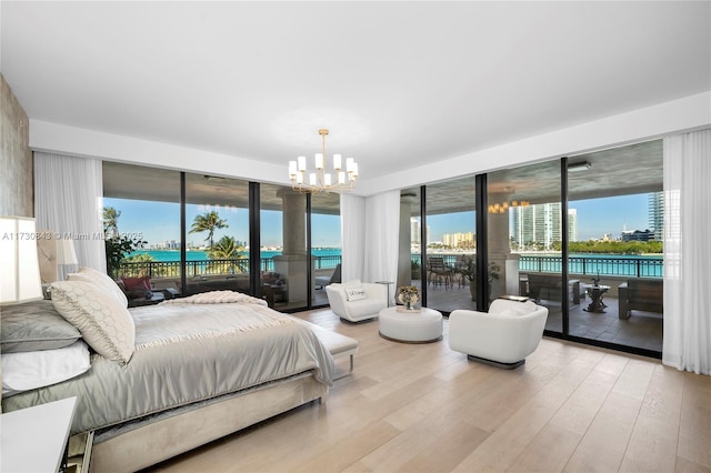 bedroom featuring a water view, a notable chandelier, light hardwood / wood-style flooring, and access to outside