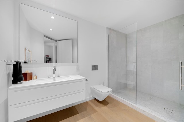 bathroom featuring hardwood / wood-style flooring, vanity, tiled shower, and toilet