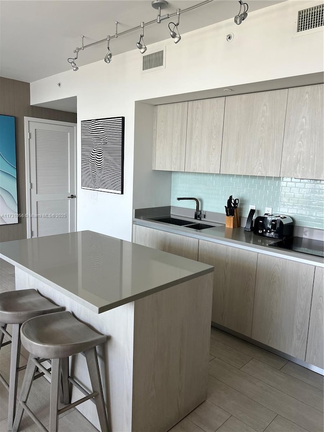 kitchen featuring sink, a breakfast bar, a kitchen island, decorative backsplash, and light brown cabinets