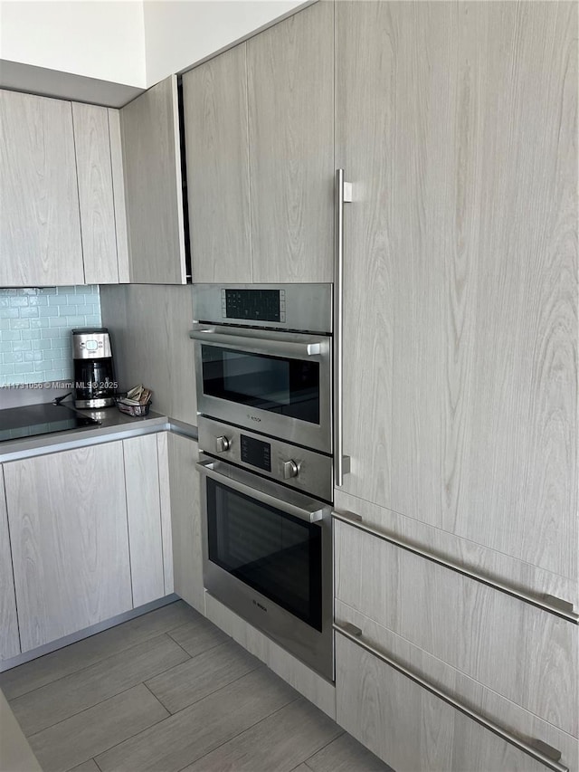 kitchen with black electric cooktop, double oven, decorative backsplash, and light brown cabinetry