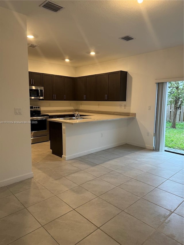 kitchen featuring light tile patterned floors, stainless steel appliances, dark brown cabinetry, a kitchen bar, and kitchen peninsula