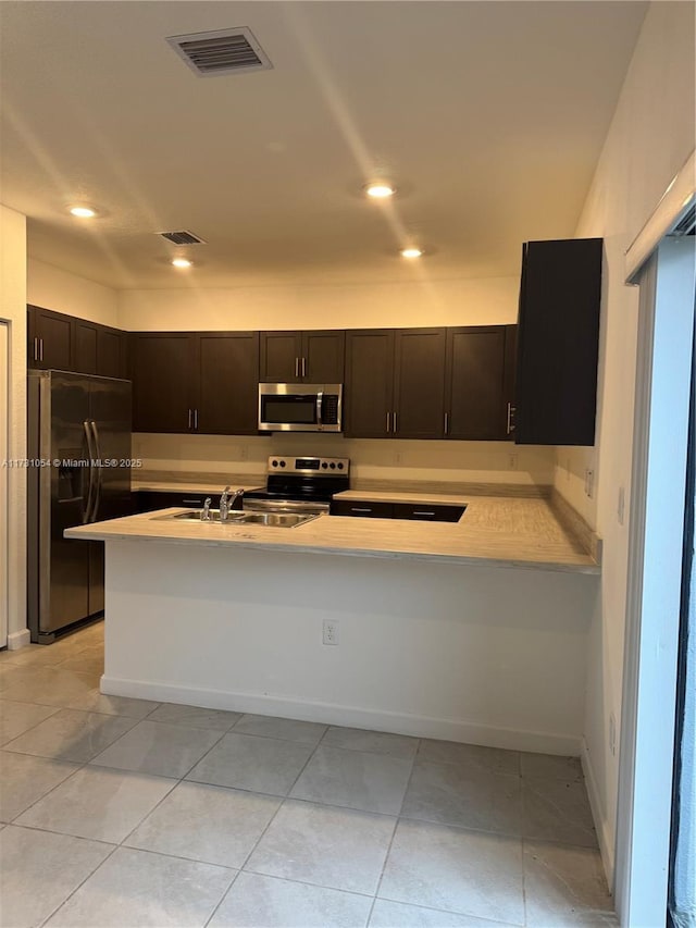 kitchen featuring light tile patterned flooring, stainless steel appliances, kitchen peninsula, and dark brown cabinets