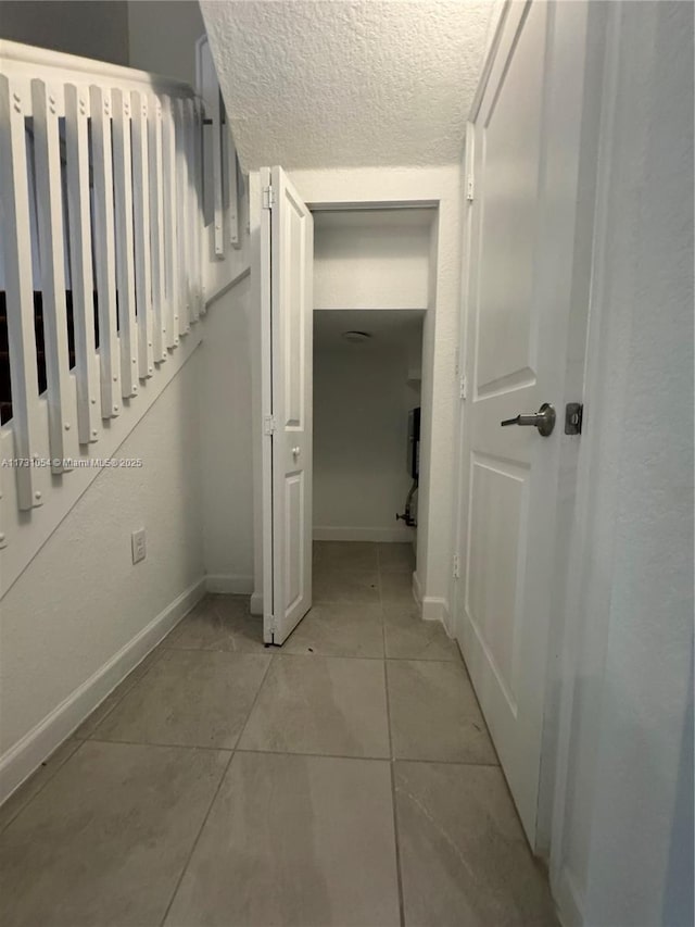 hallway with a textured ceiling and light tile patterned floors