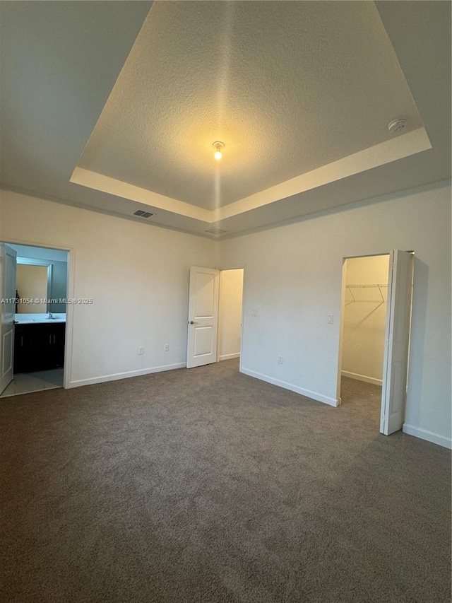 unfurnished bedroom featuring connected bathroom, a spacious closet, a tray ceiling, a closet, and carpet