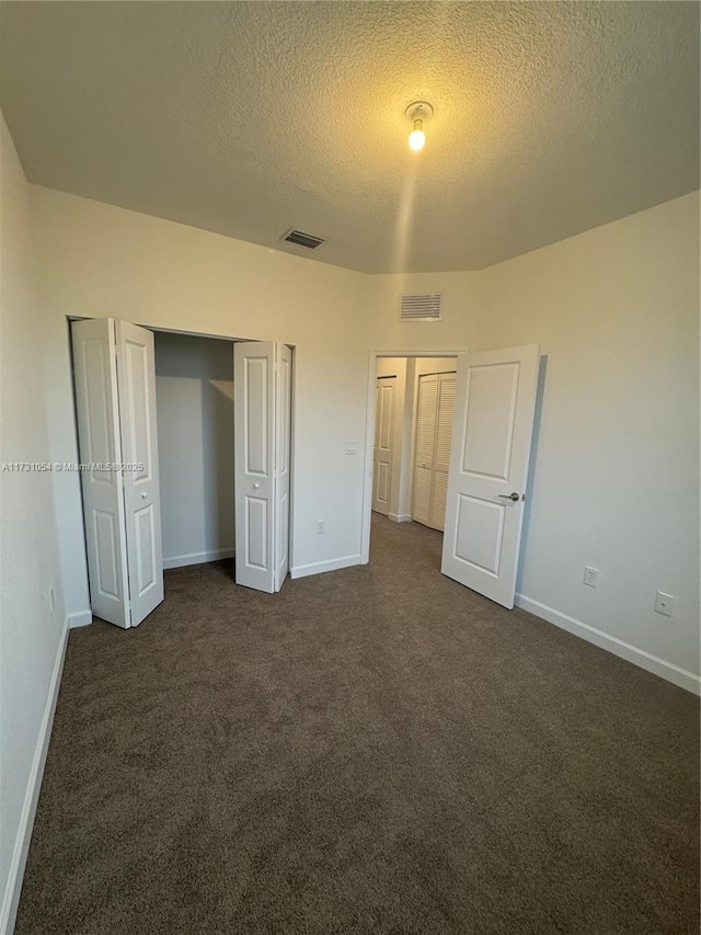 unfurnished bedroom with dark colored carpet and a textured ceiling