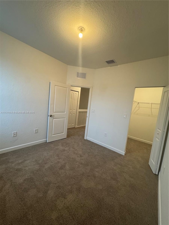 unfurnished bedroom featuring a spacious closet, a textured ceiling, a closet, and dark colored carpet