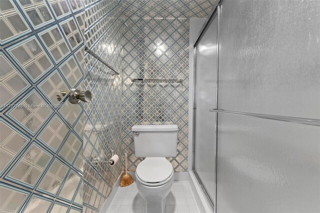 bathroom with tile walls, toilet, a shower with door, and tile patterned flooring