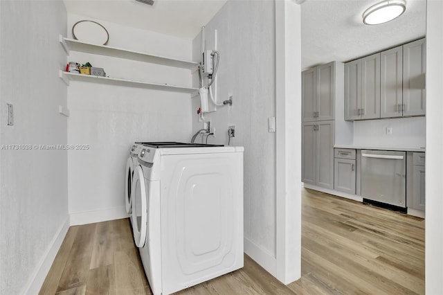 laundry area with washing machine and clothes dryer, a textured ceiling, light hardwood / wood-style floors, and cabinets