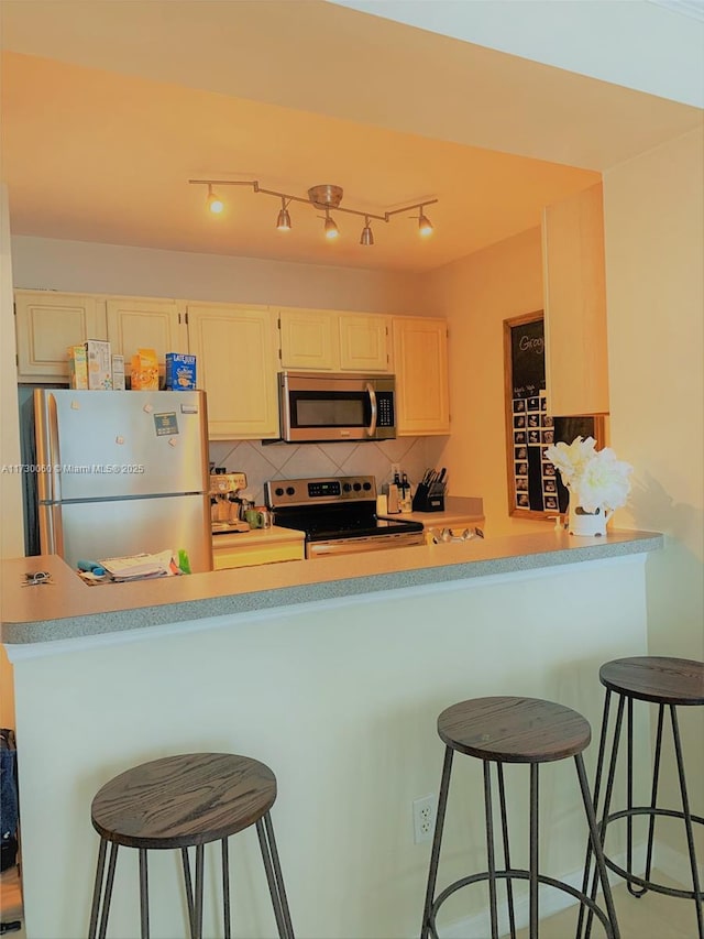 kitchen with stainless steel appliances, kitchen peninsula, a kitchen breakfast bar, and backsplash