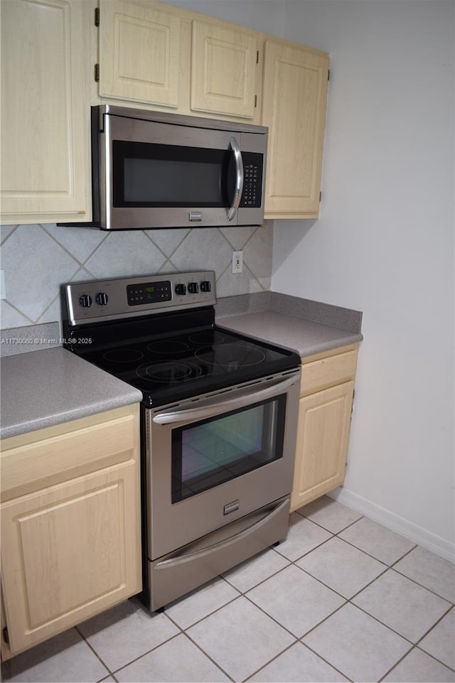 kitchen with light tile patterned floors, stainless steel appliances, baseboards, backsplash, and light brown cabinets