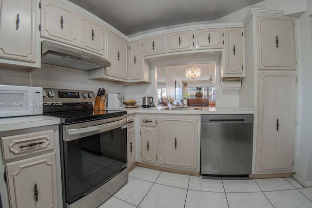 kitchen with appliances with stainless steel finishes, sink, tasteful backsplash, light tile patterned floors, and a chandelier