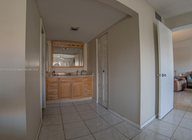 hall with sink, a textured ceiling, and light tile patterned floors