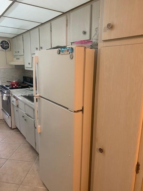 kitchen with light tile patterned floors, gas stove, visible vents, premium range hood, and freestanding refrigerator