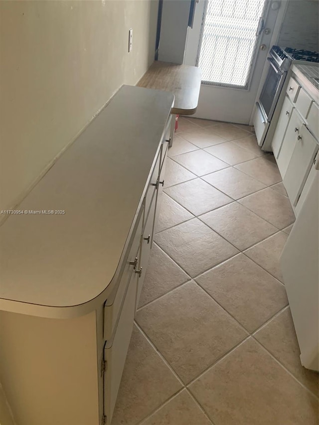 kitchen with light tile patterned flooring, stainless steel range with gas stovetop, and white cabinets