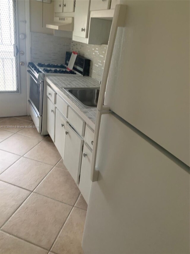 kitchen with white appliances, ventilation hood, light tile patterned floors, tile counters, and backsplash
