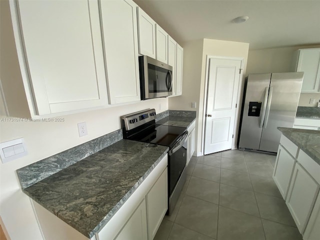 kitchen featuring stainless steel appliances, dark tile patterned floors, dark stone counters, and white cabinets