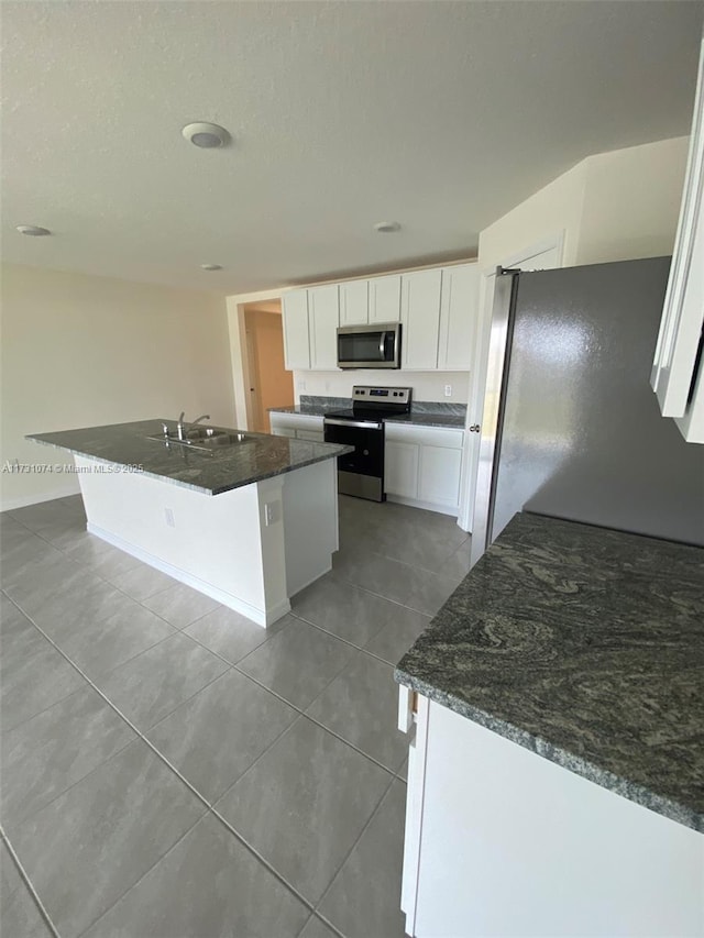 kitchen with white cabinetry, stainless steel appliances, dark stone countertops, and a center island with sink