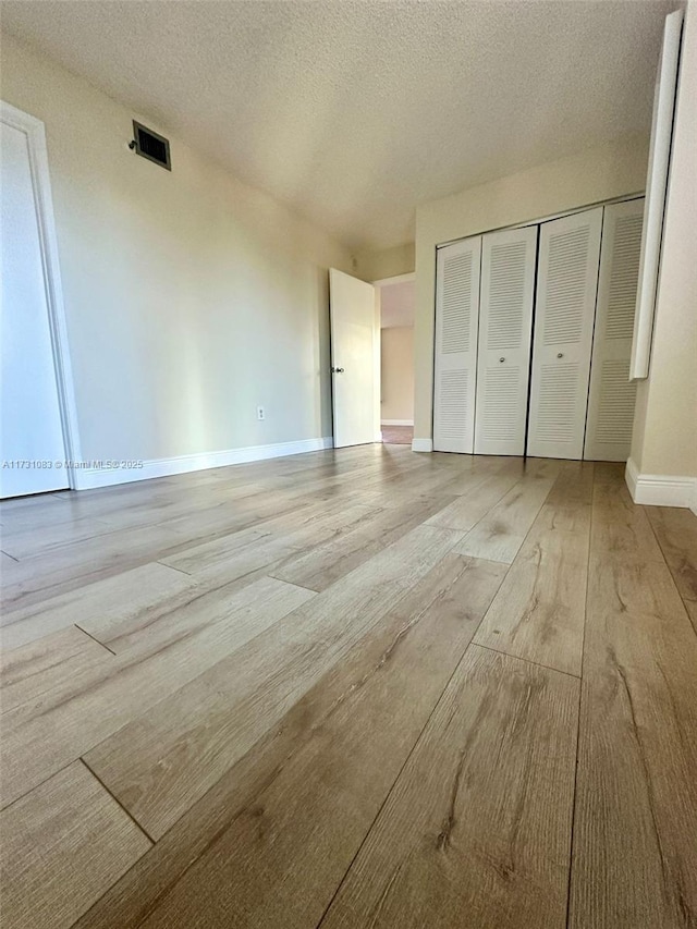 unfurnished bedroom with a textured ceiling, light wood-type flooring, and a closet