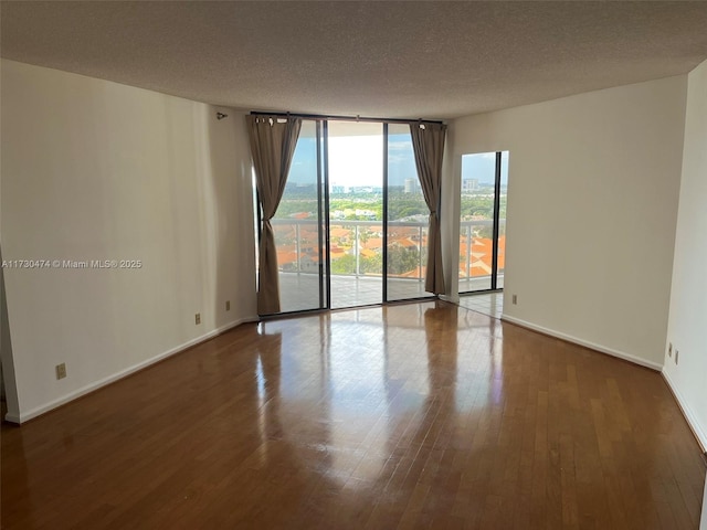 empty room featuring wood-type flooring, a textured ceiling, and a wall of windows