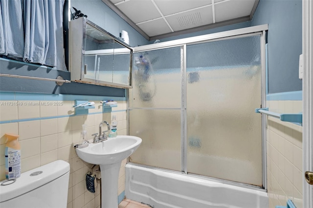 bathroom featuring combined bath / shower with glass door, toilet, and tile walls