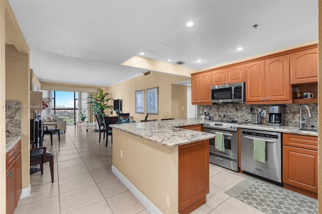 kitchen with appliances with stainless steel finishes, tasteful backsplash, kitchen peninsula, light stone counters, and light tile patterned floors